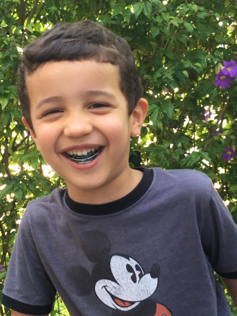 Imagem de um menino com plantas ao fundo. A criança está sorrindo e usando um aparelho nos dentes.